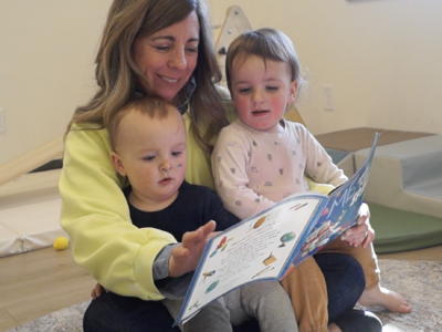 Missy sits with two toddlers and reads to them.