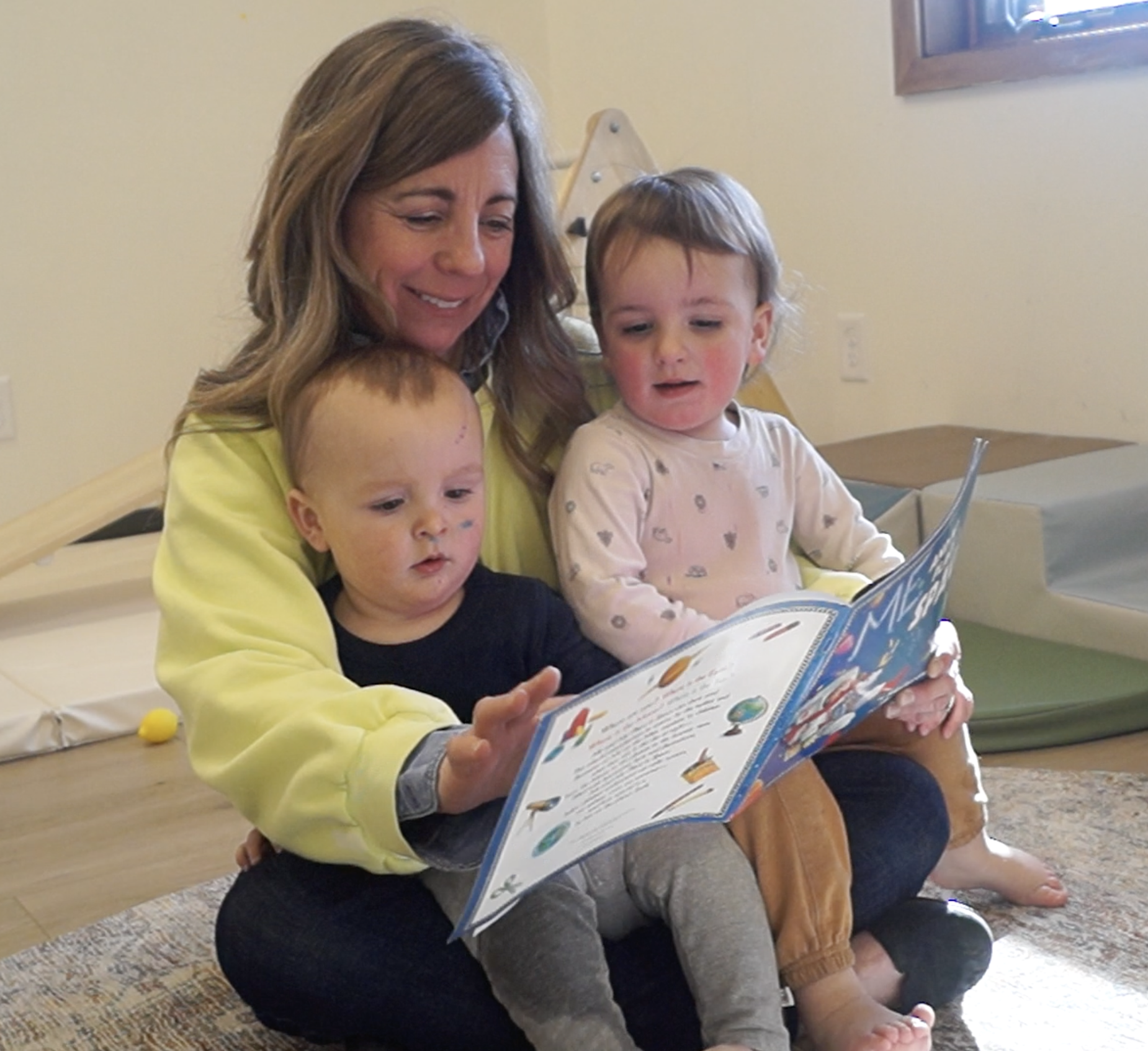 Missy sits with two toddlers and reads to them.